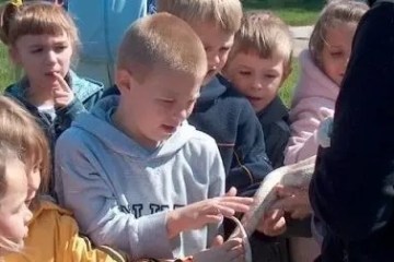 Children gathered around an adult, some touching a snake.